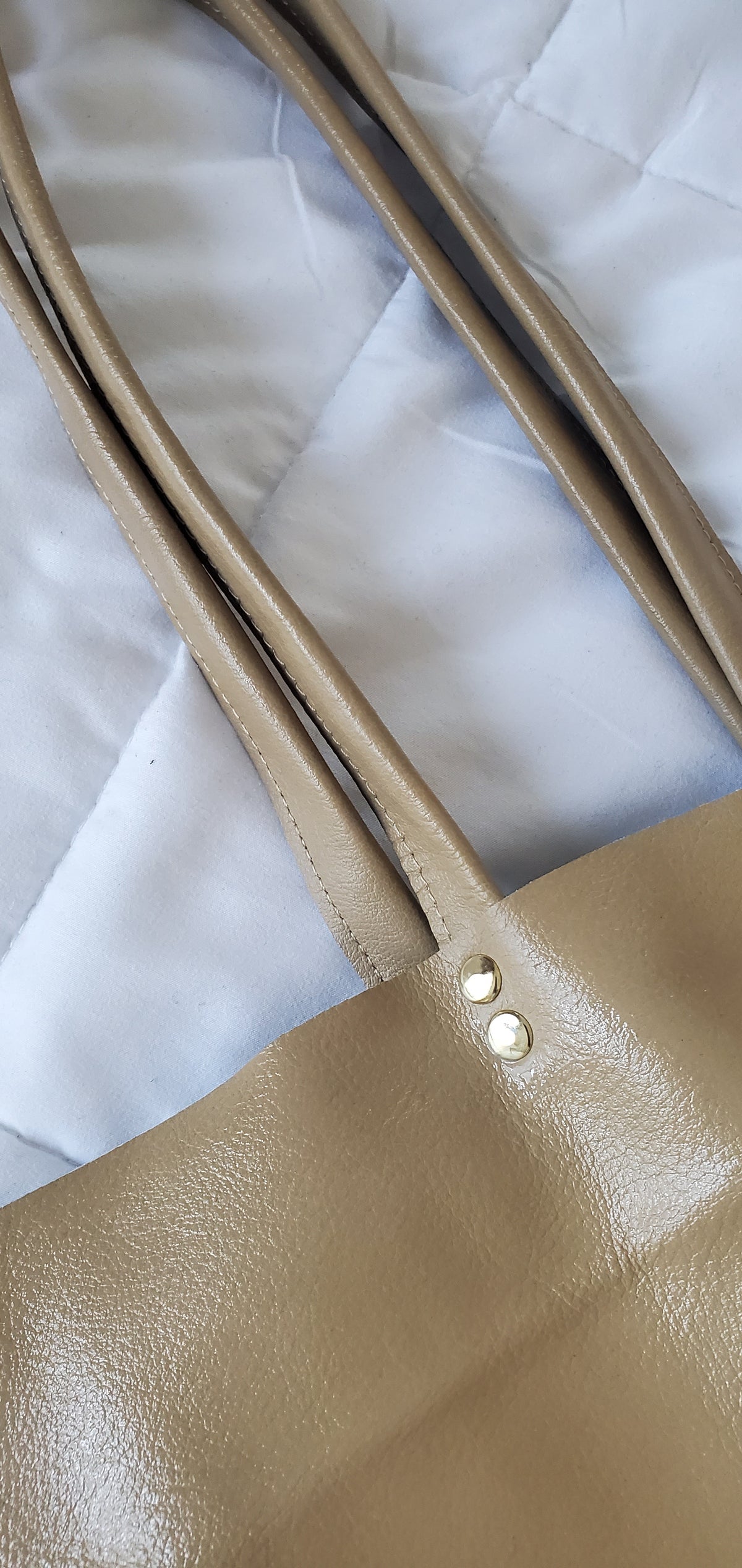 Close-up of a beige leather handbag with visible stitching on a white background